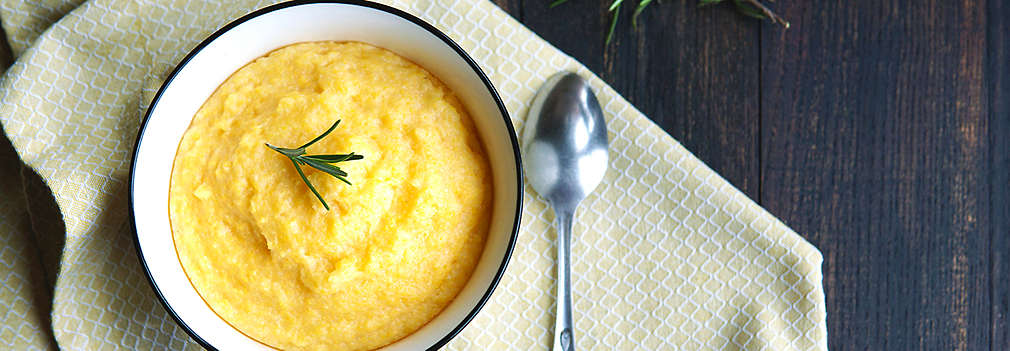 Polenta dekoriert mit einem kleinen Rosmarinzweig in einer weißen Schale auf einem Esstisch