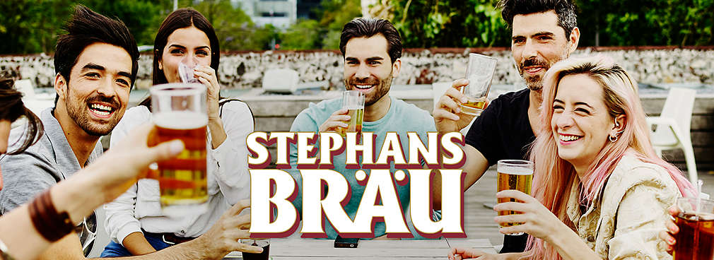 Mehrere Personen stoßen mit einem Glas Bier im Biergarten an; Logo: STEPHANS BRÄU