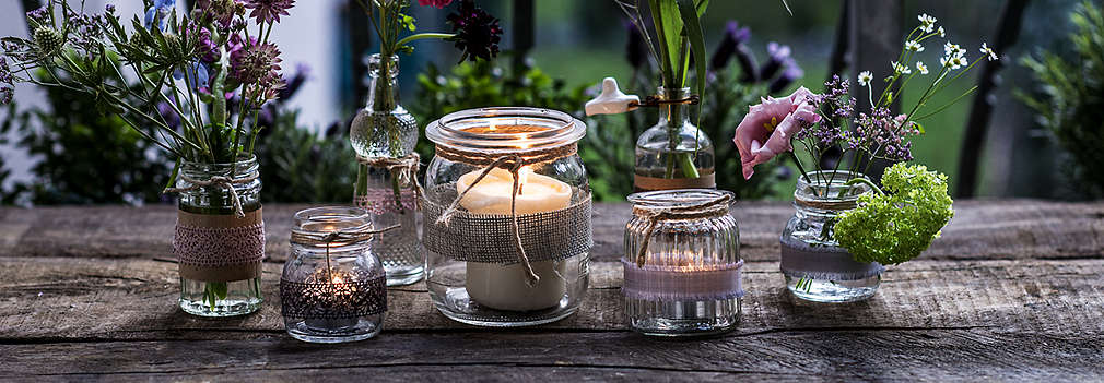 Изображение на стъклени Countryside® свещници и вазички с цветя на дървена повърхност