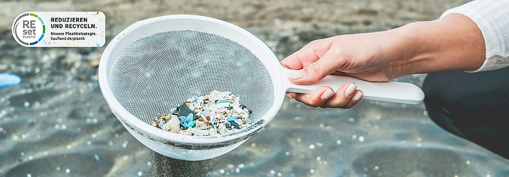 Hand hält Kescher mit kleinen Steinen und Mikroplastikteilchen