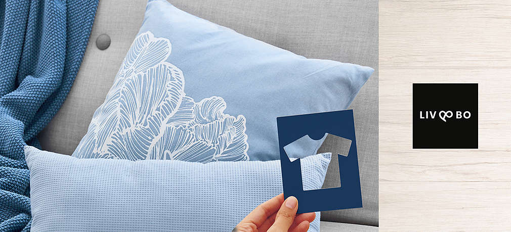 hellblaue Kissen und Decke, davor eine Schaplone mit T-Shirt-Ausschnitt; Logo: Liv & Bo®