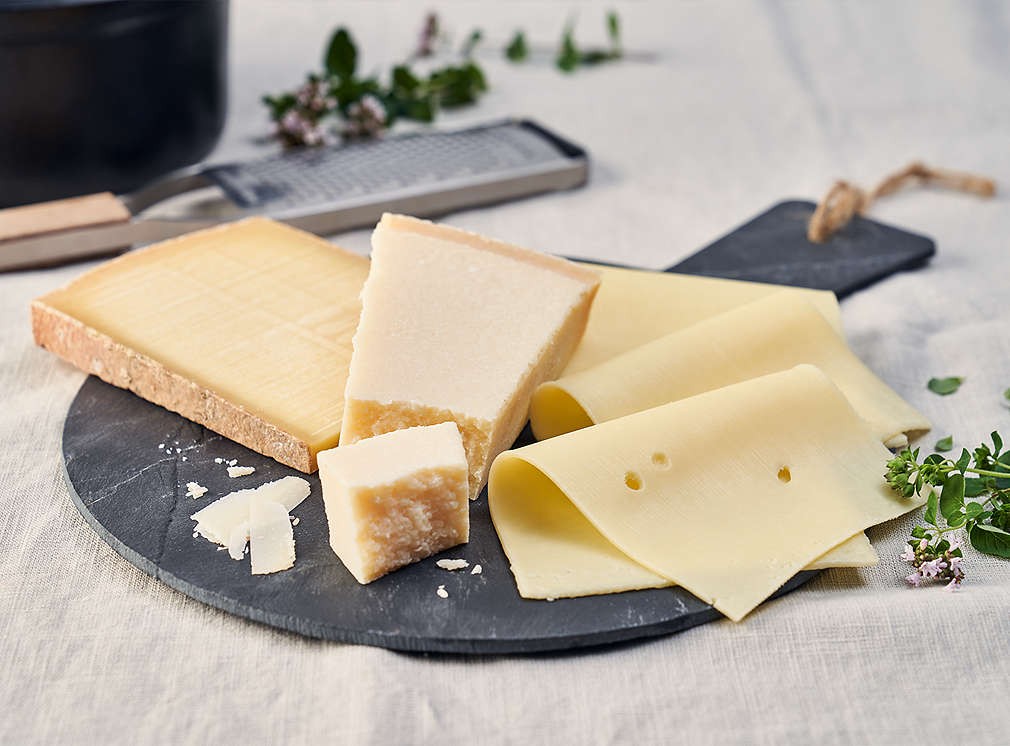 Tvrdý sýr nakrájený na plátky, struhadlo na sýr a bylinky.