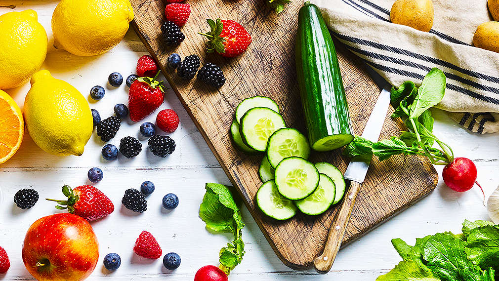 Stół, na którym leży drewniana deska z owocami i warzywami