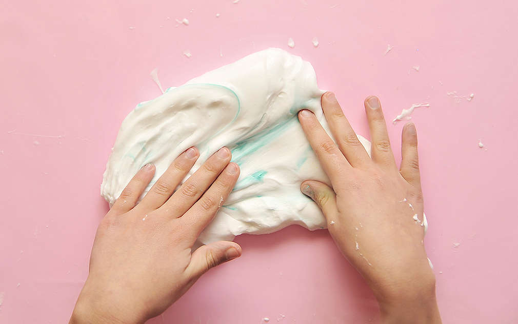 Снимани отгоре детски ръце, които омесват бяла маса с малко синя боя.