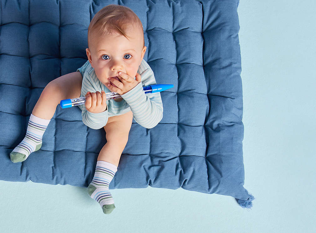 Baby sitting on pillow, looking up and playing with oversized pencil.​,Baby sitting on pillow, looking up and playing with oversized pencil.?