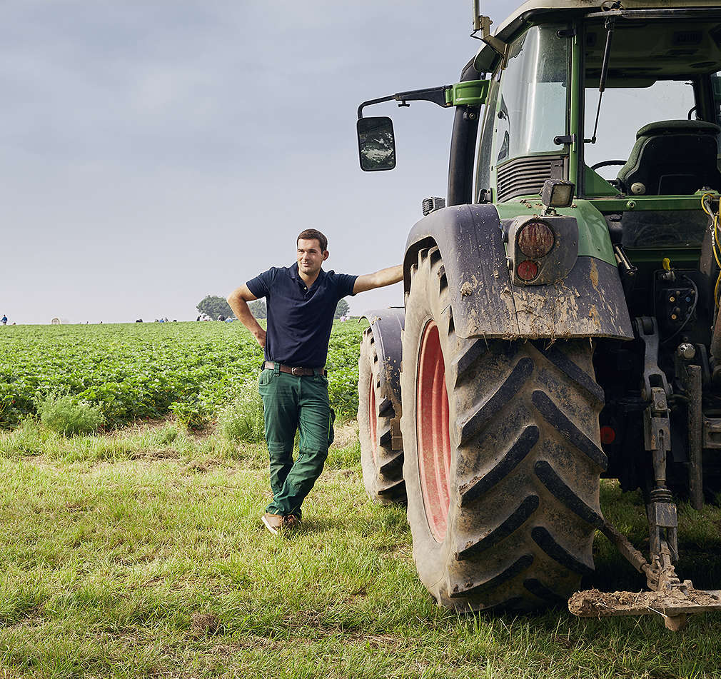 Farmář se opírá o traktor zaarkvoaný na poli