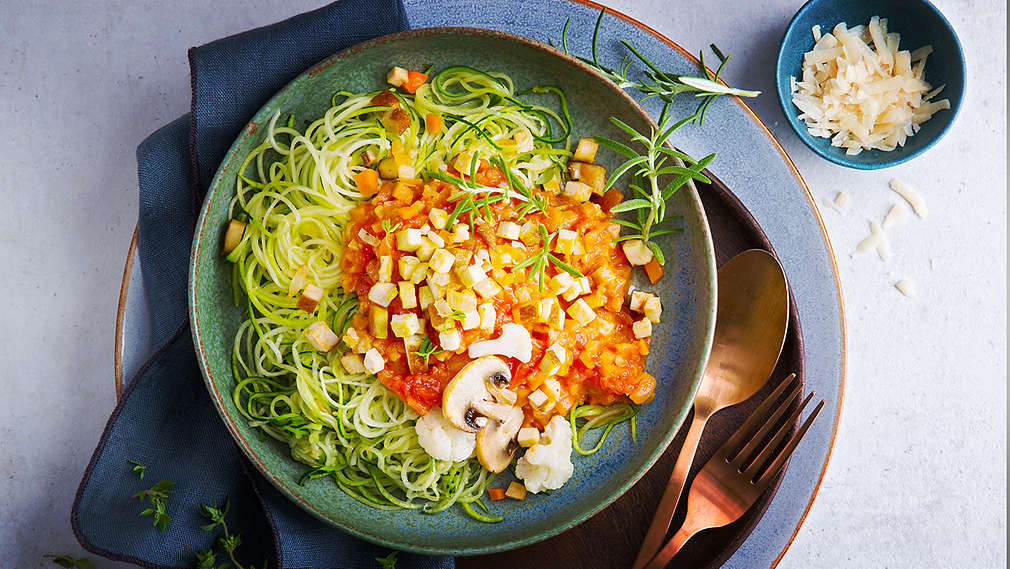 O farfurie cu paste din zucchini fotografiată de sus, cu diferite legume și tofu.