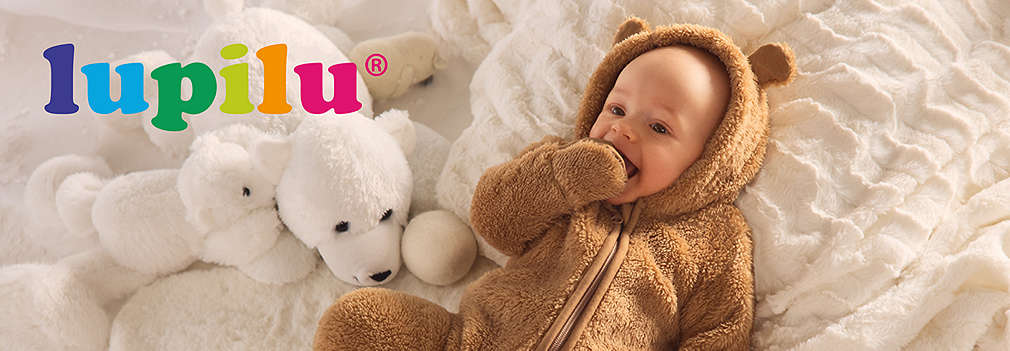 Ein lachendes Baby trägt einen flauschigen braunen Lupilu Fleece-Overall mit Öhrchen an der Kapuze und liegt auf einer weichen weißen Decke neben einem Eisbär-Kuscheltier., Ein lachendes Baby tr�gt einen flauschigen braunen Lupilu Fleece-Overall mit �hrchen an der Kapuze und liegt auf einer weichen wei�en Decke neben einem Eisb�r-Kuscheltier.