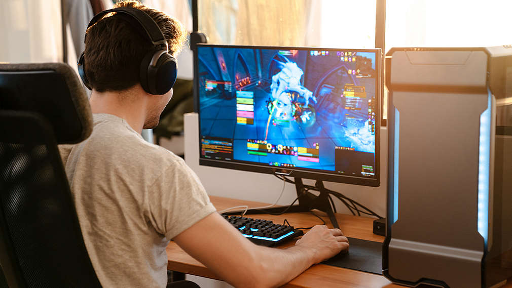 Молодой человек сидит за письменным столом и играет в компьютерную игру.