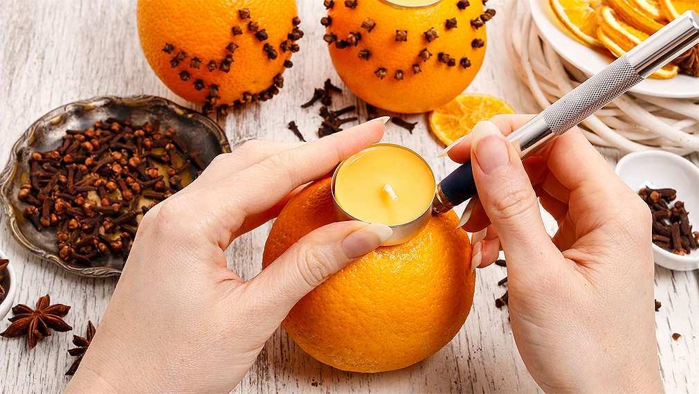 Dve ženské ruky upravujú pomaranč do formy svietnika. V miske na stole sú klinčeky na dozdobenie svietnika.