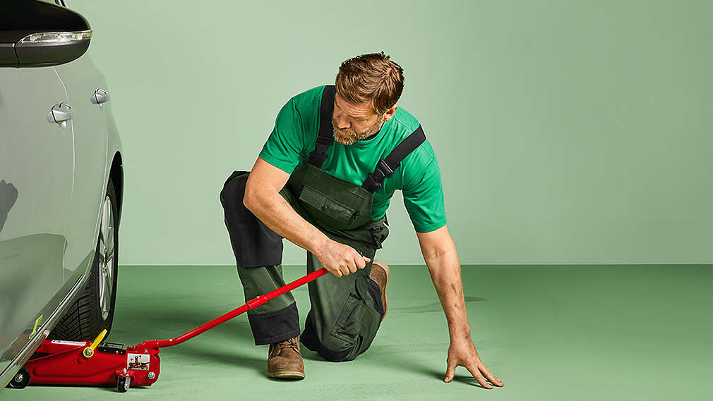 Muž zvedá své auto zvedákem, aby následně vyměnil pneumatiky.
