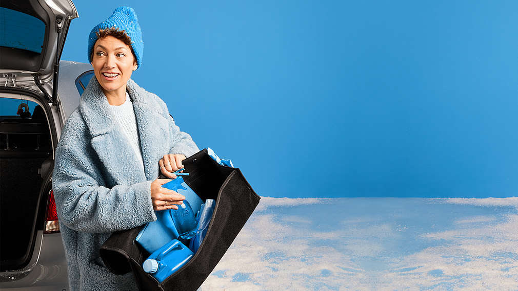 Žena stojí před otevřeným šedým autem a v ruce drží tašku s různými produkty MyProject.