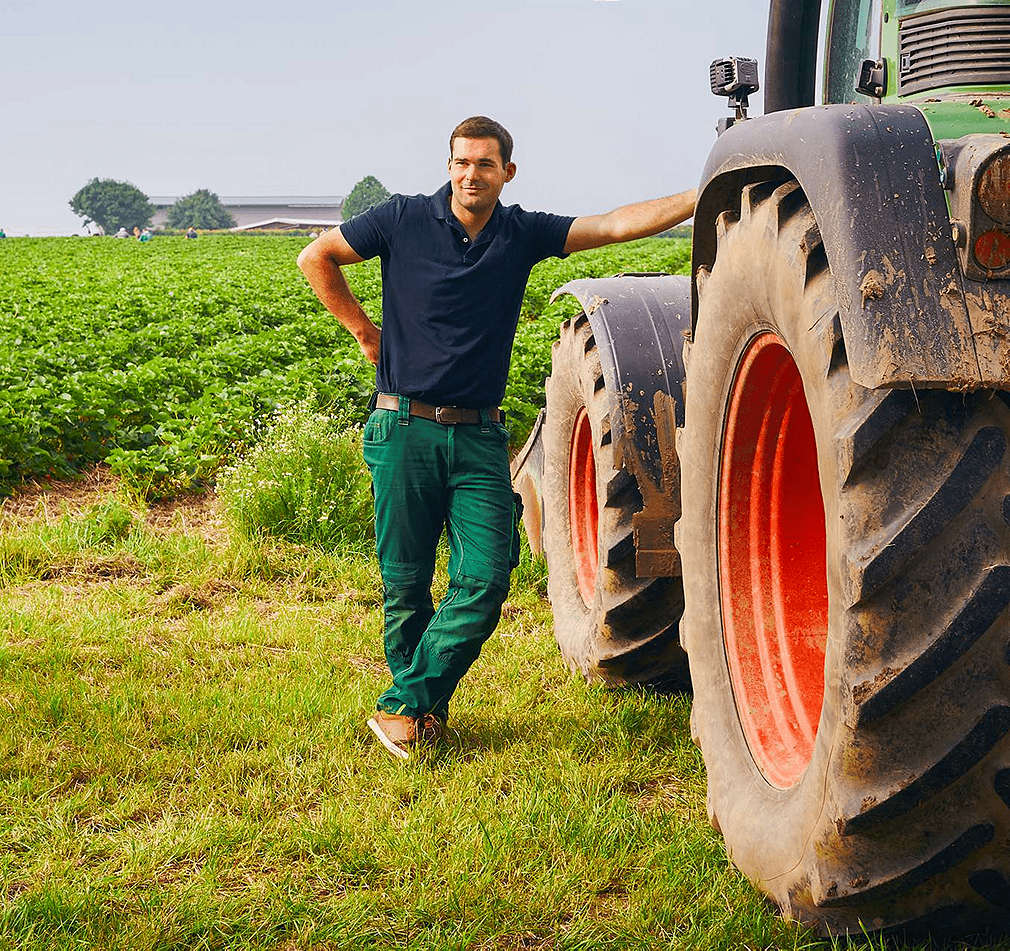 Bauer lehnt sich an Traktor auf einem Feld