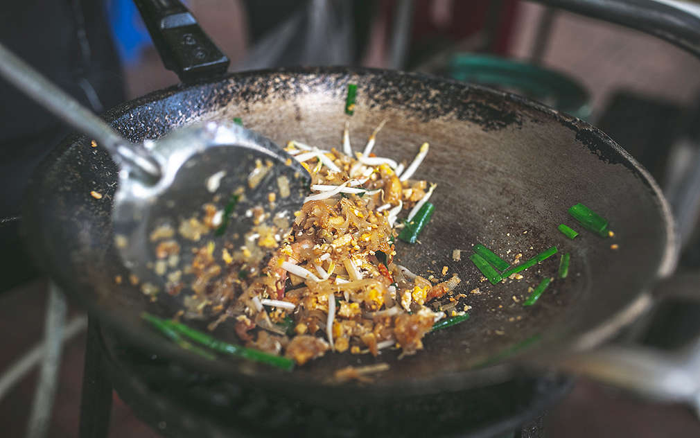 Pánev wok, ve které se právě čerstvé ingredience na pad thai míchají obracečkou, aby se aromata promíchala.