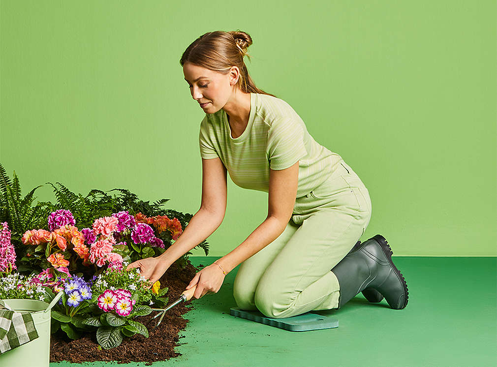 A woman plants colorful flowers. The scenery is placed on a green background.