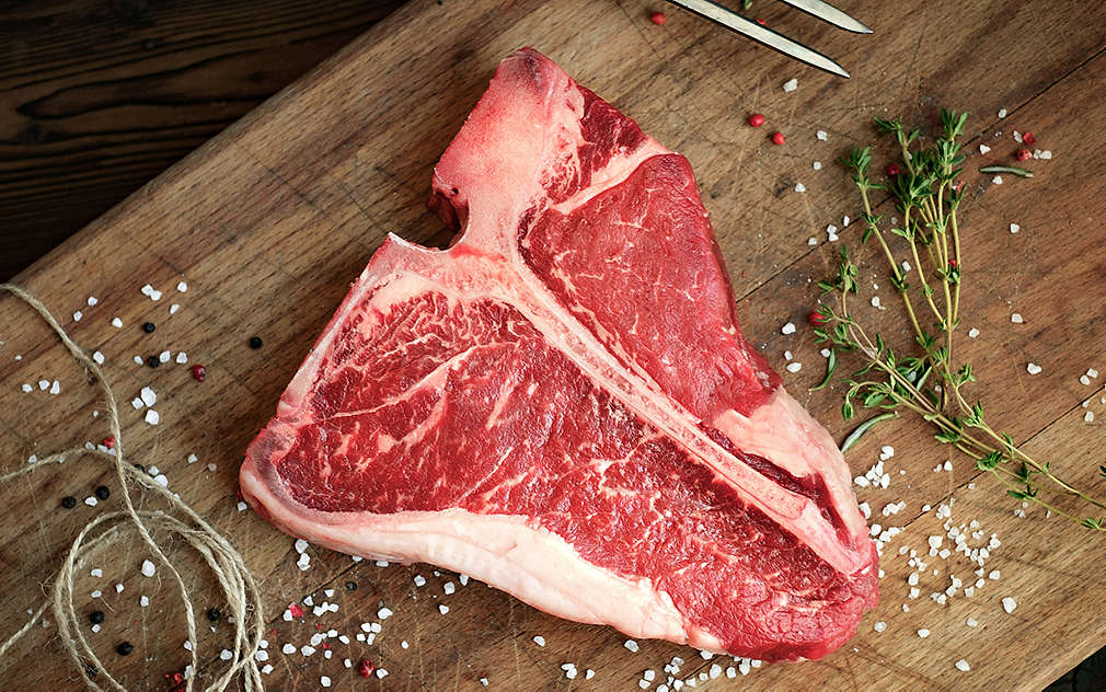 Можете да видите сурово парче месо върху дървена кухненска дъска  – със сол и други подправки.