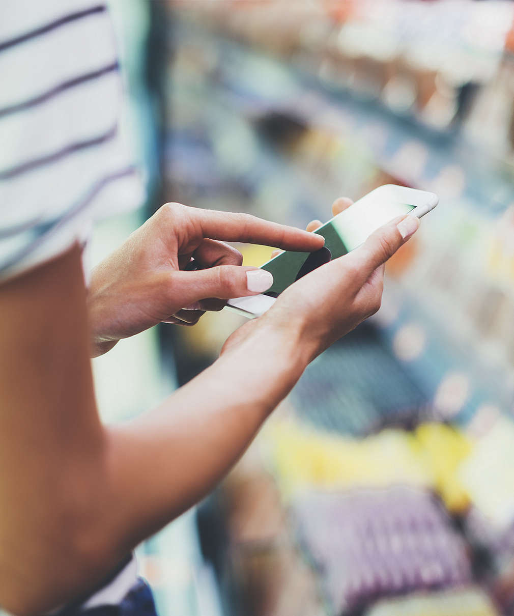 Woman with mobile phone in front of a refrigerated shelf