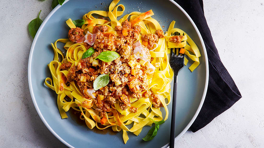 Na jasnym blacie leży czarna serwetka. Na niej stoi talerz z bolognese.