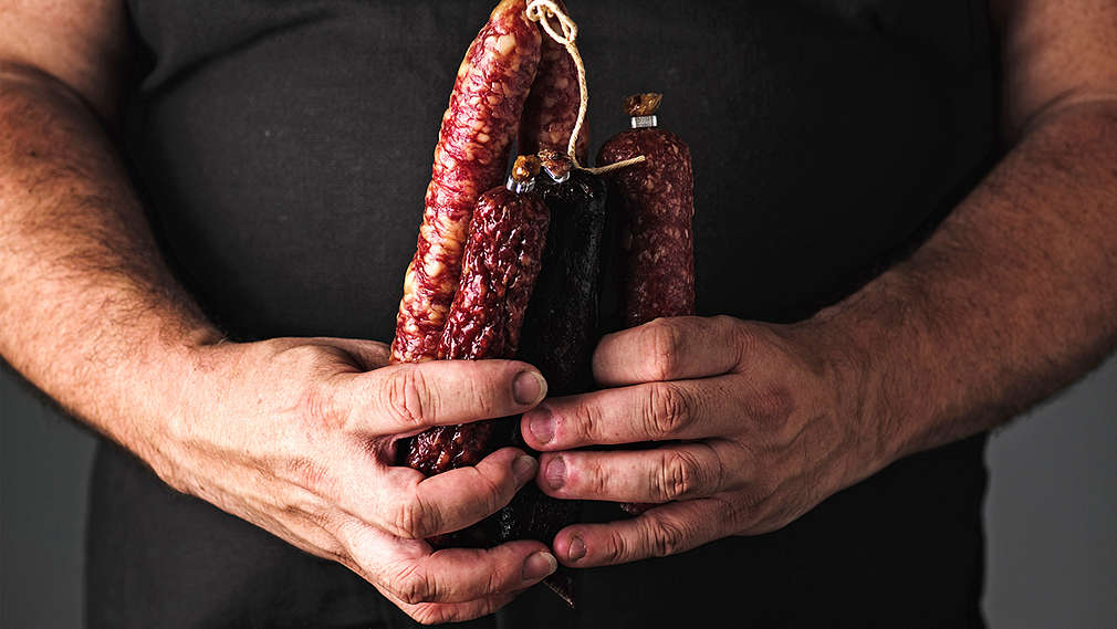 Muž drží v ruce klobásy.