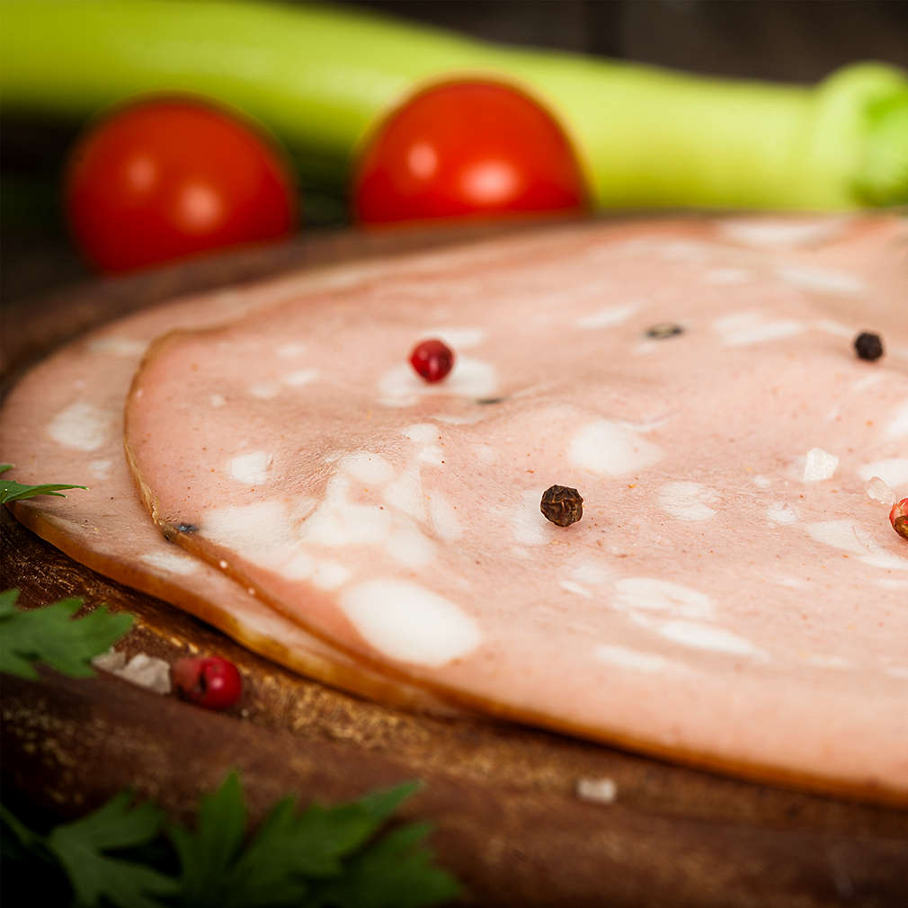 Italian mortadella salami on wooden board with tomato and green pepper 