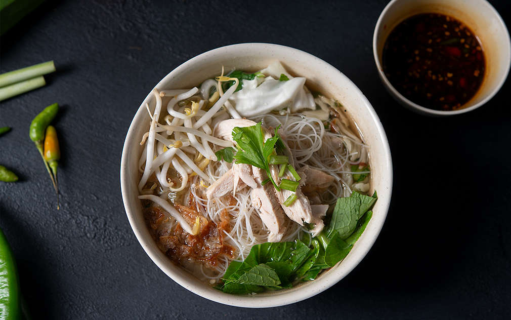 Polévkové jídlo s rýžovými nudlemi je naservírováno v misce a vedle stojí sojová omáčka.