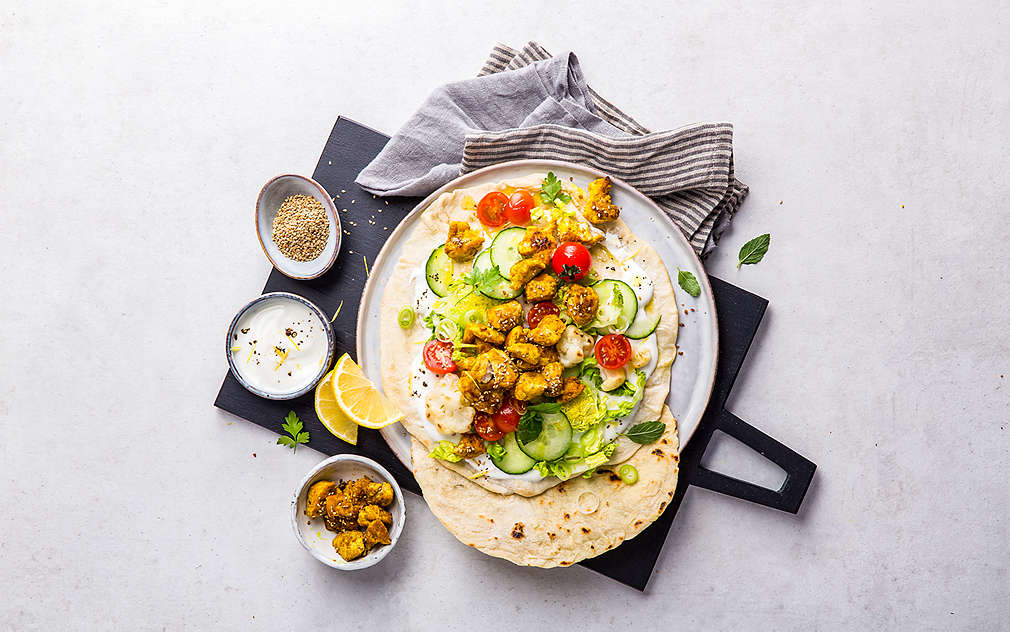 Поставена табела на таблото за обяви. В чинията има питки, гарнирани с дип, резени краставица, чери домати, маруля и мариновано тофу на скара. Отстрани на чинията е поставена кухненска кърпа на сини и бели райета, а над нея – три малки купички с мариновано тофу, дип и сусам, както и две резенчета лимон.