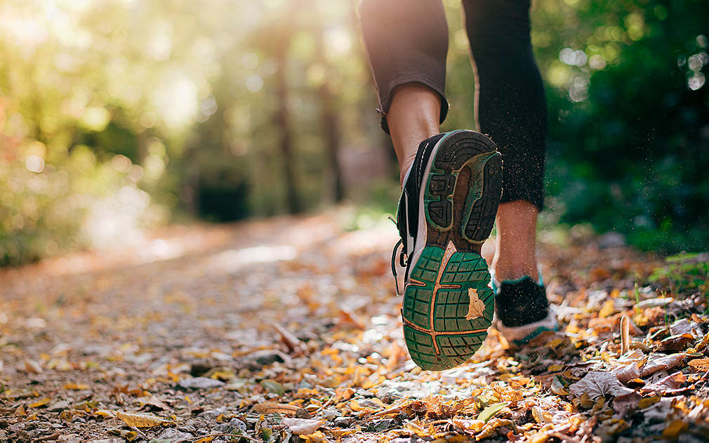 Šljunčani puteljak na kojem se vide noge i tenisice žene koja trči, dok se u pozadini mutno vide livada i pejzaž.