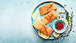 Tri komada lososa pripremljena na okruglom tanjuru. Oko njih se nalaze kriške limuna i začini.