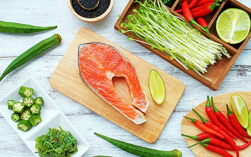 O bucată de somon crud pe un platou de lemn, înconjurat de legume.