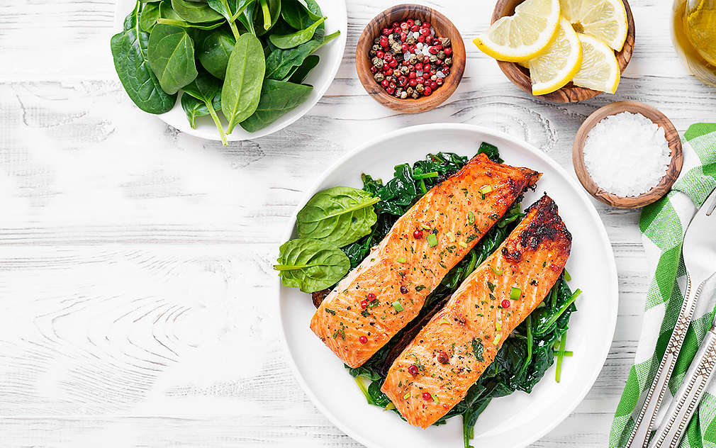 O bucată de pește servită pe o farfurie, alături de frunze de spanac.