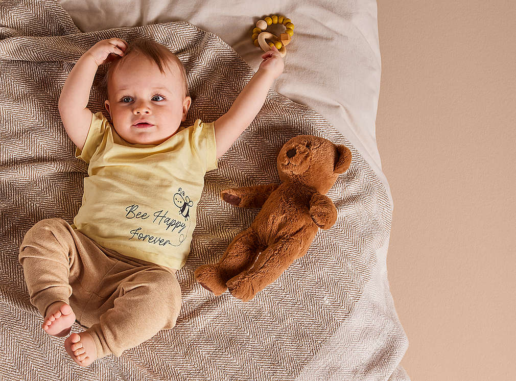 Abbildung: Baby liegt mit einem Teddy auf einer Decke