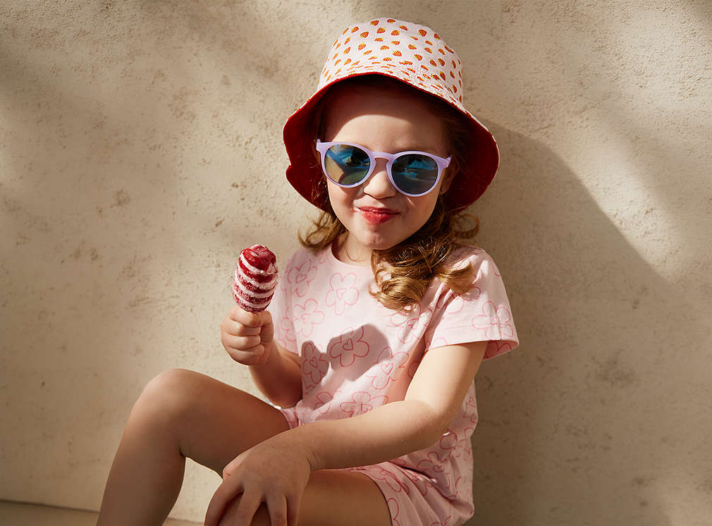 Kind mit Sonnebrille, Hut und einem Eis in der Hand