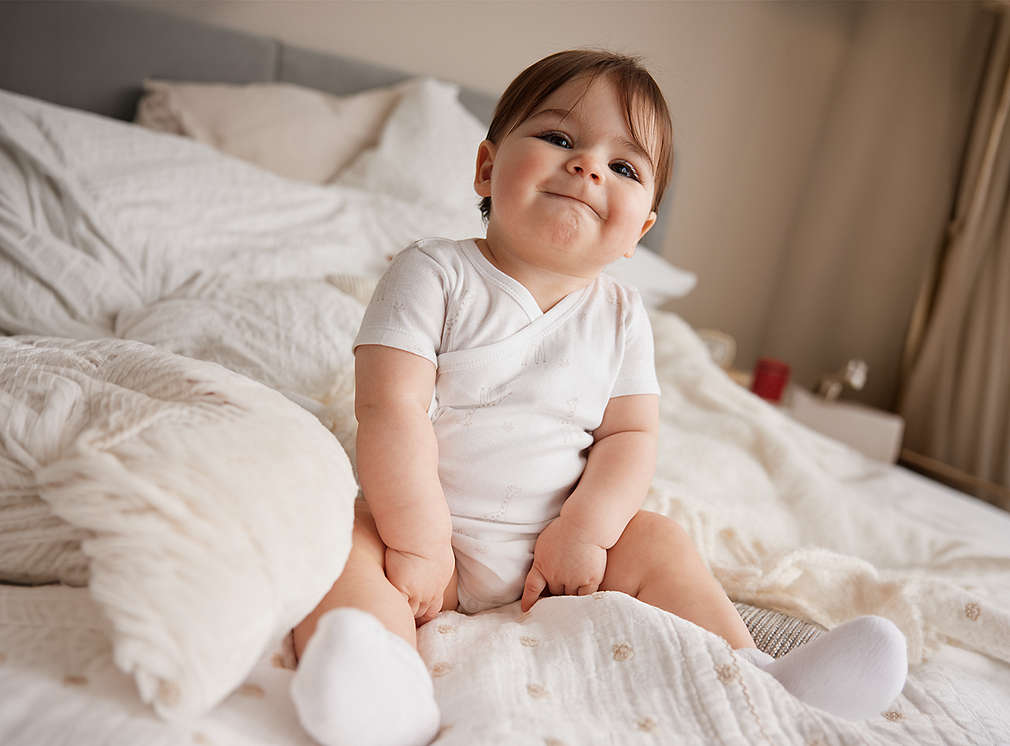 Baby sitzt auf einem Bett