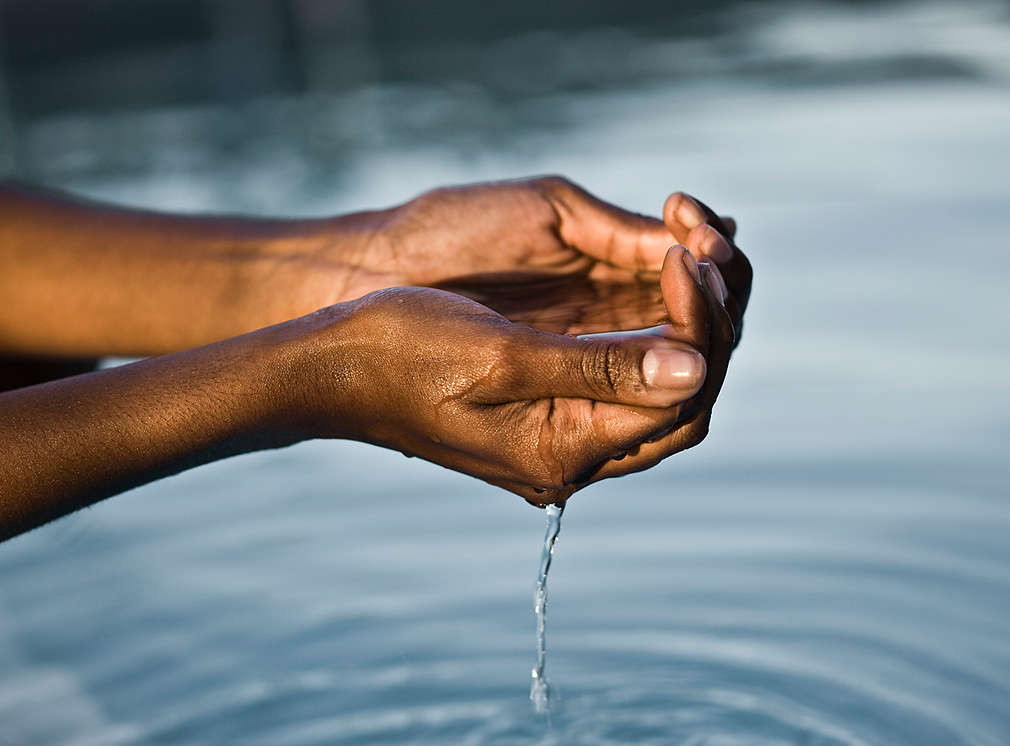 ruce držící vodu nad hladinou jezera