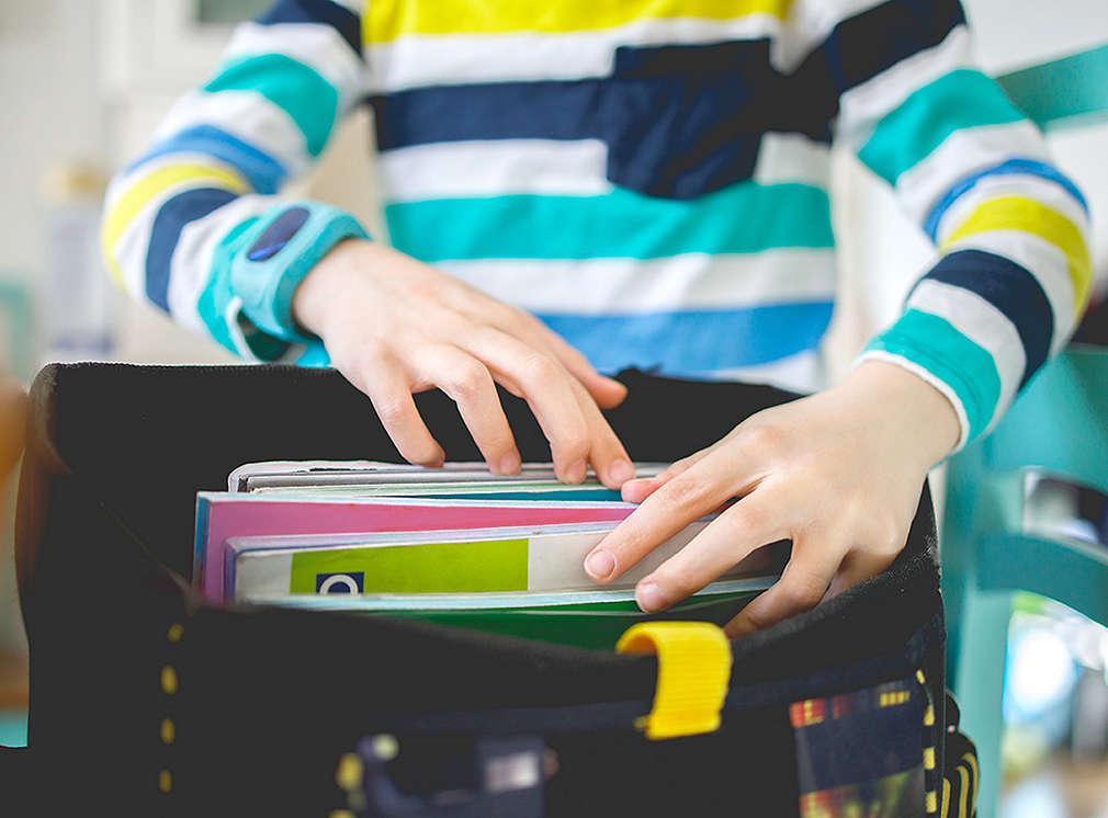 Schulkind packt seinen Schulranzen mit verschiedenen Heften und Büchern