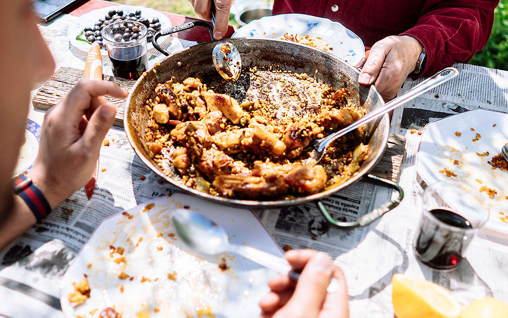 Tava s paellom valencianom nalazi se na stolu. Jedna osoba jede je žlicom ravno iz tave.