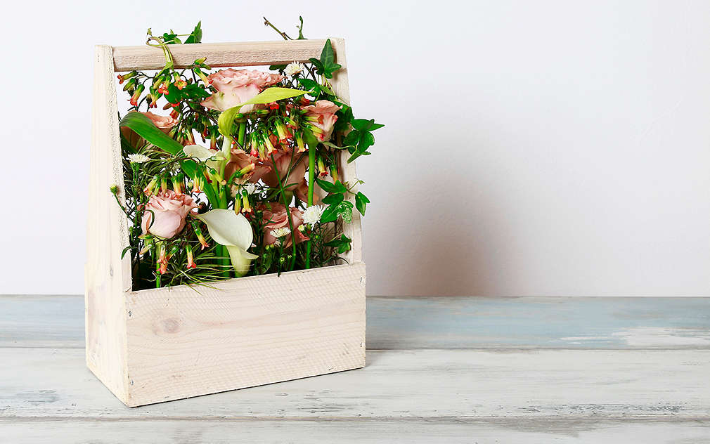 Bielo lakovaná drevená plocha, na nej stojan na fľaše, ktorý je naplnený jarnými kvetmi.