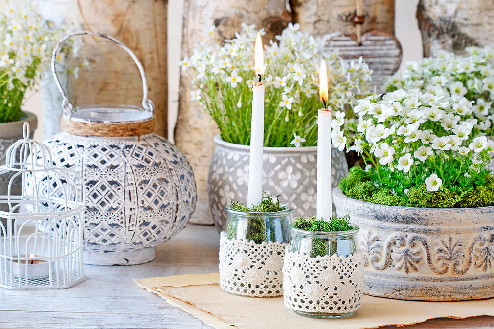 Stół na którym stoją doniczki, kosze i słoiki ozdobione koronką
