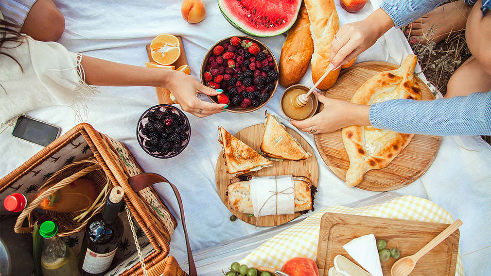 Изображение на одеало за пикник, върху което са подредени различни храни