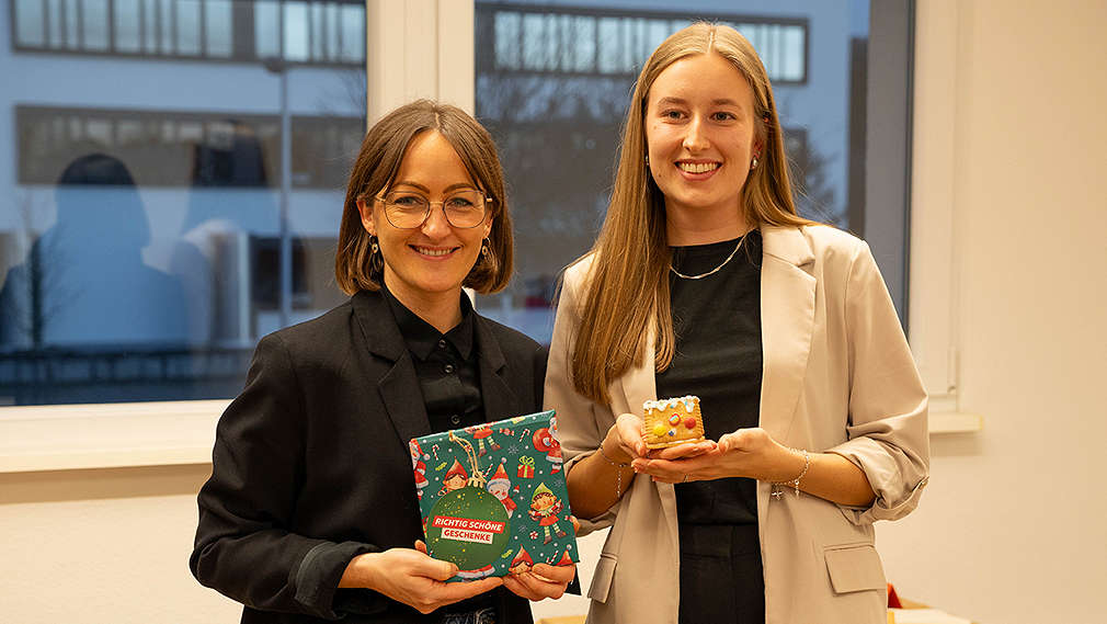 Zwei Frauen mit einem Geschenk in der Hand lächeln in die Kamera
