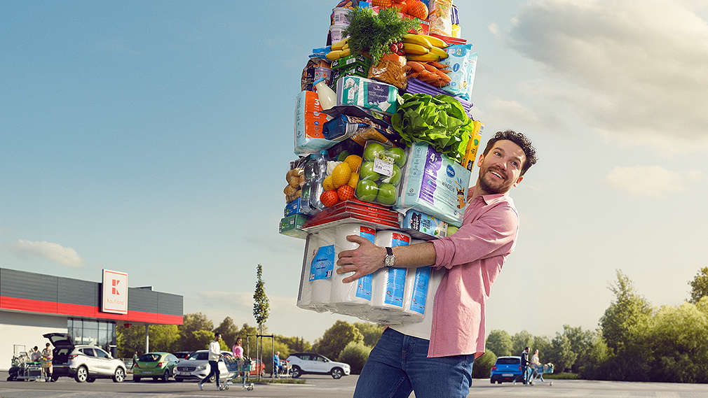 Mann vor einer Kaufland-Filiale mit verschiedene Produkte aus den Bereichen Frische, Grundnahrungsmittel, Drogerie und Getränke
