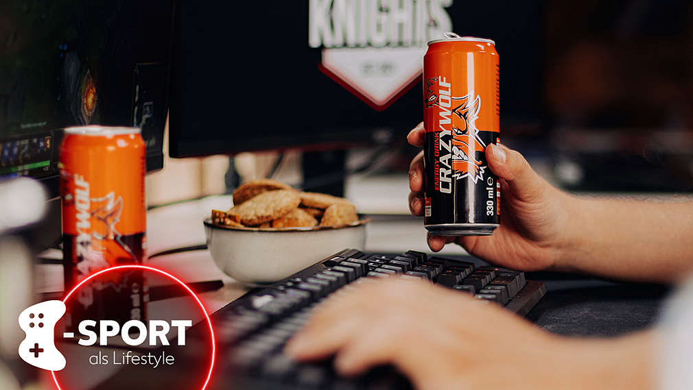 Person sitzt am Schreibtisch und spielt Videospiele; zu sehen ist eine beleuchtete Gaming-Tastatur, ein Gaming-Bildschirm im Anschnitt, zwei Energydrinks und ein Schälchen mit Crackern