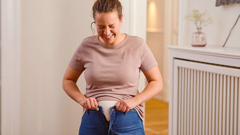 Lächelnde Frau, die ihre Jeanshose nicht mehr zu bekommt