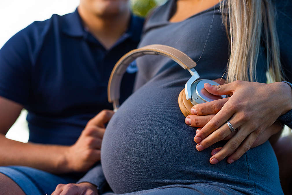 Изображение на корем бременна жена, на който са поставени слушалки