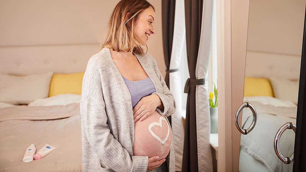 Werdende Mutter betrachtet ihren Babybauch vor dem Spiegel 
