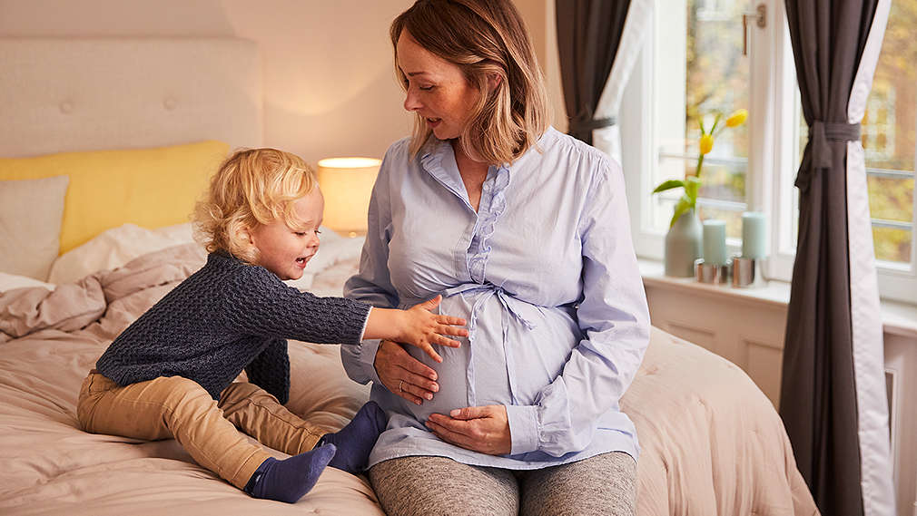 Erstgeborener legt Hand auf den Babybauch der Mutter