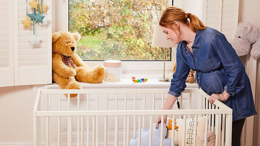 Schwangere Frau legt Kissen in ein Babybett