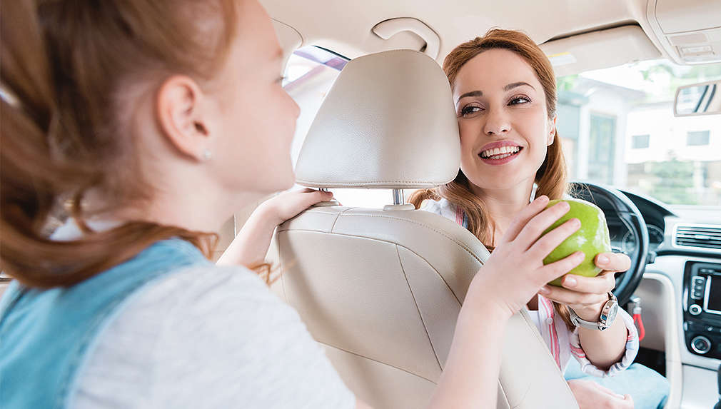 Mutter reicht Kind einen Apfel im Auto