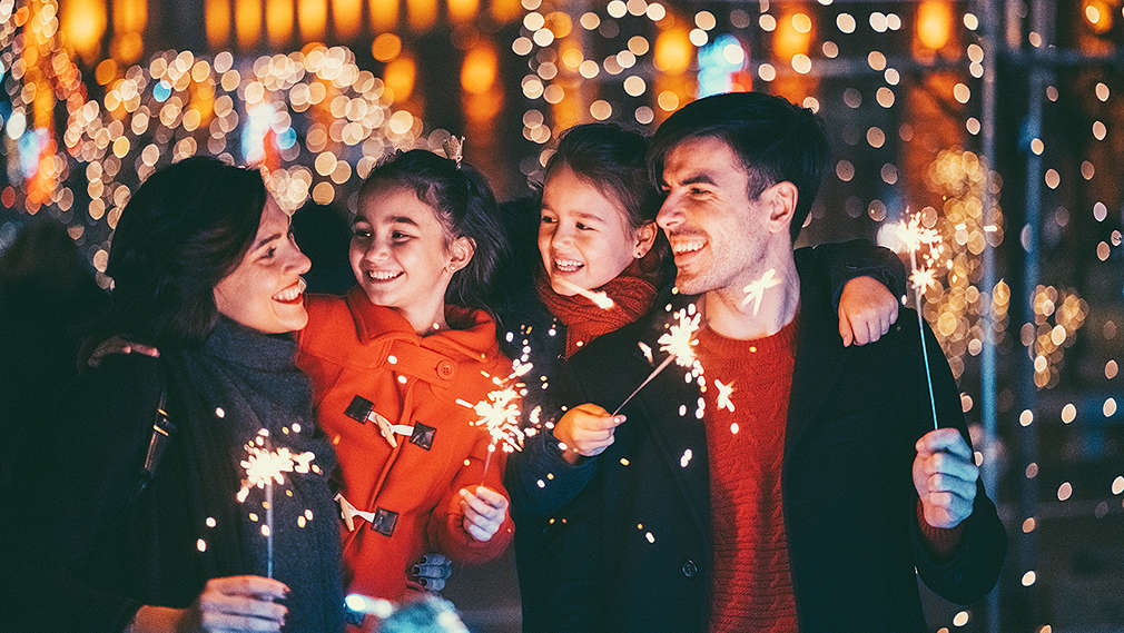 Eltern mit Kindern feiern draußen Silvester mit Wunderkerzen