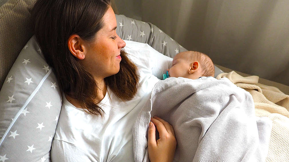 Mutter liegt mit ihrem neugeborenen Kind im Bett
